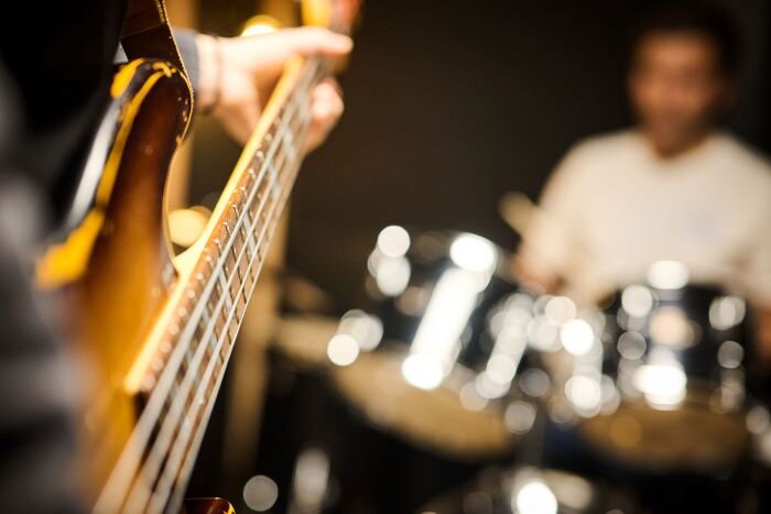 Close-up of an aged wood bass neck with drums in the background. | © Plug The Jack
