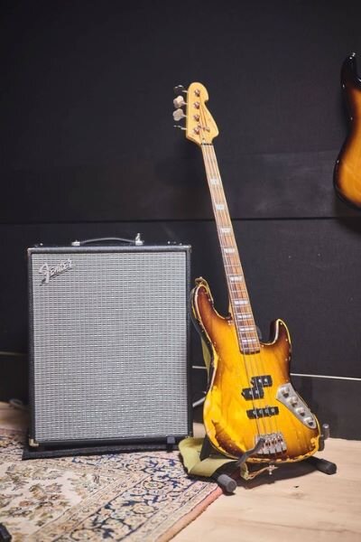 Basse en bois vieilli contre un ampli Fender Rumble 200 dans studio de répétition. | © Plug The Jack
