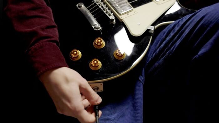Zwarte gitaarbody met koperen knoppen en arm die een jack met de gitaar verbindt. | © Plug The Jack