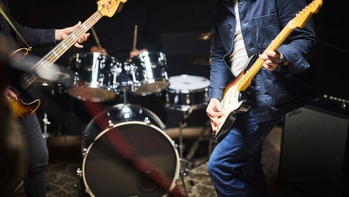 Rock band aan het repeteren in een muziekrepetitieruimte met bassist, gitarist en drummer. | © Plug The Jack
