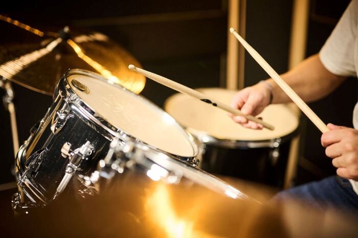 Drummer in actie met stokken in een muziekrepetitiestudio. | © Plug The Jack